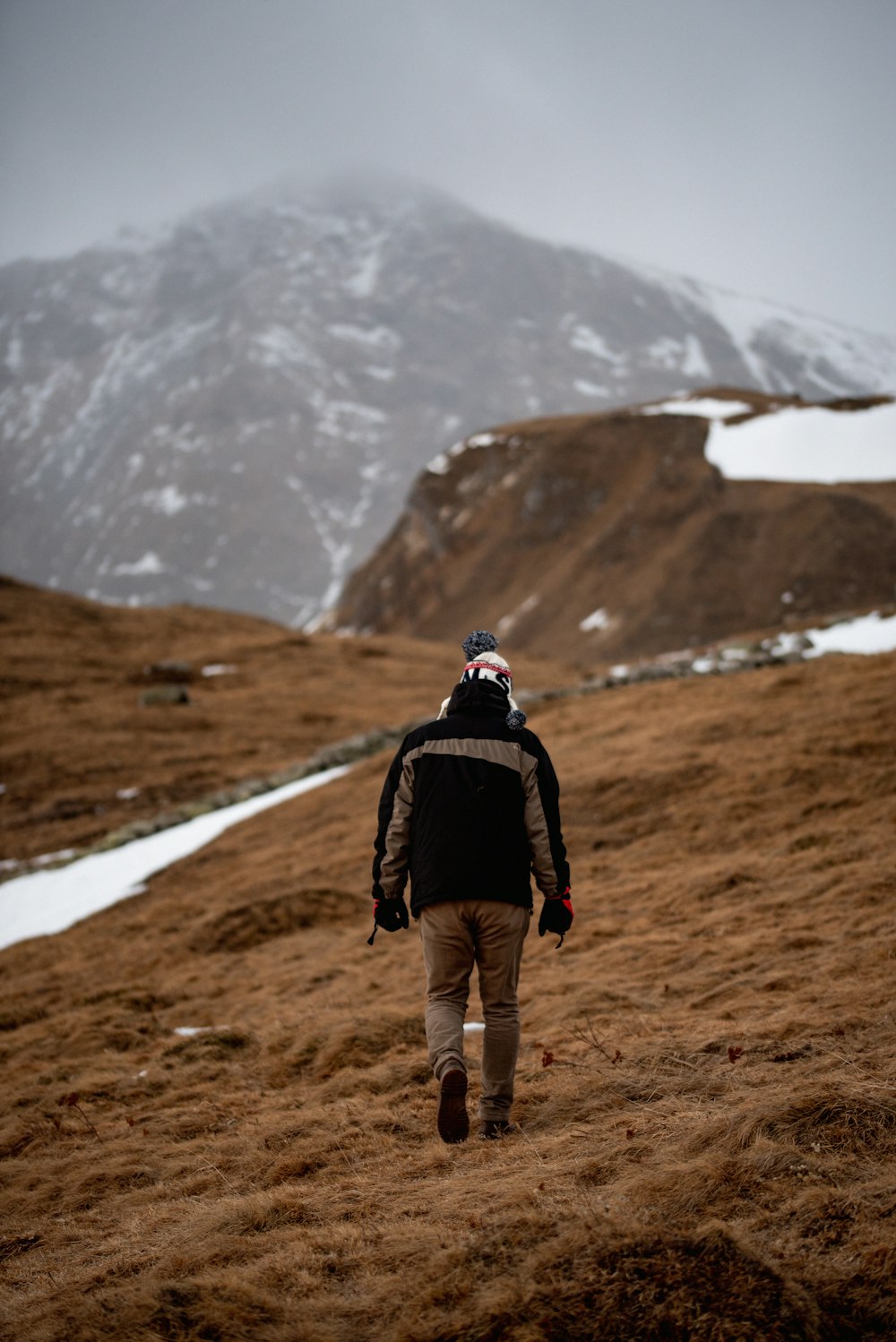 a man walking up a hill with a snow covered mountain in the background