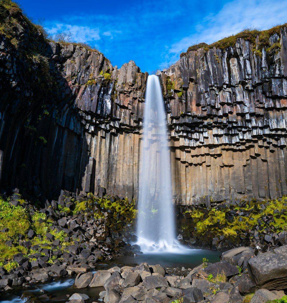 a large waterfall is surrounded by rocks and greenery