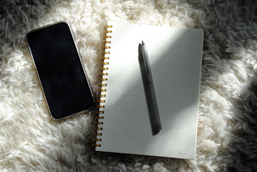 a notepad, pen, and phone on a fluffy surface