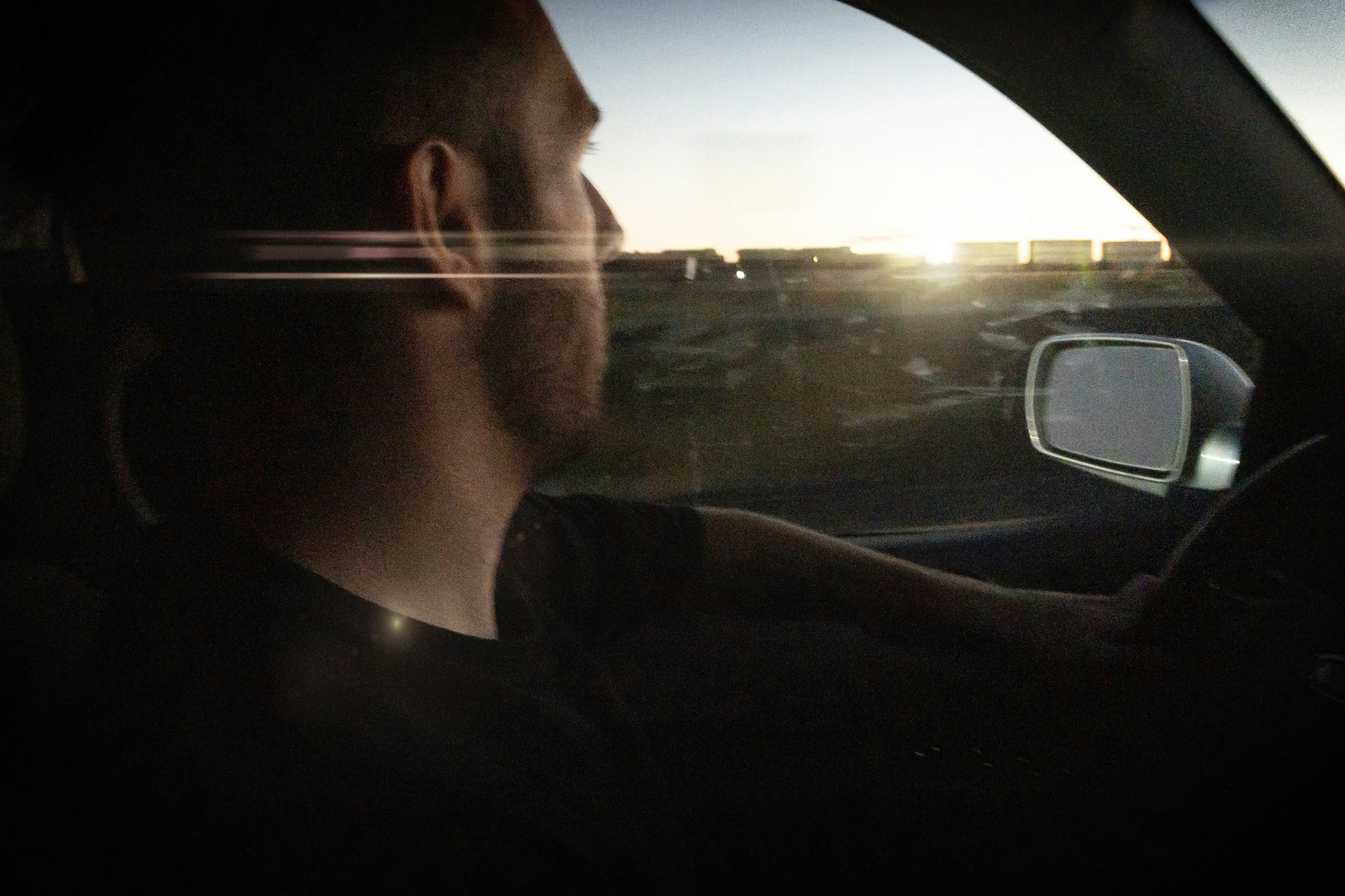 Man driving car towards sunset with lens flare
