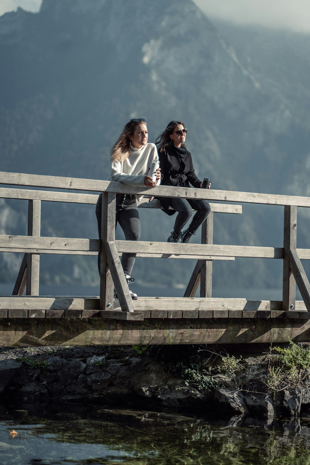 two women sitting on a wooden bridge over a body of water