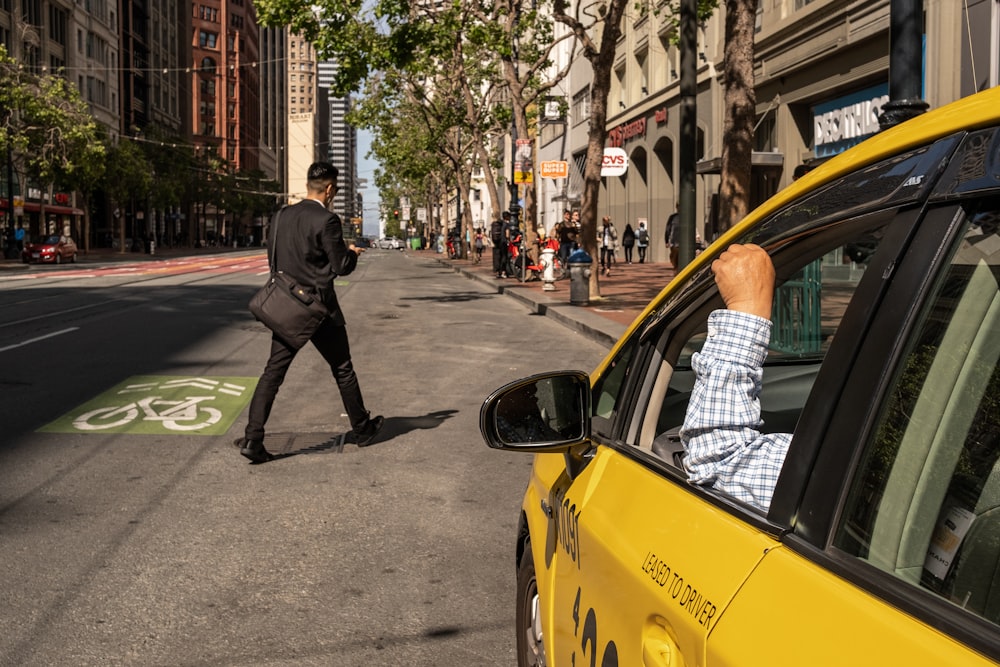 a man walking across a street next to a yellow car