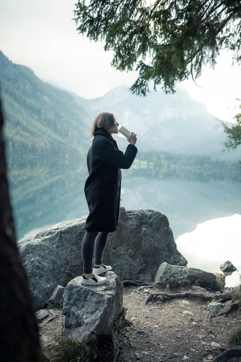 a woman standing on top of a rock next to a lake