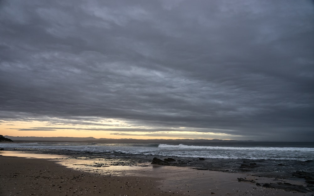 a cloudy day at the beach with a surfboard in the foreground