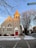 A church with light gray siding and a red door stands at the corner of a street. The architecture includes large arched windows with decorative designs. Bare trees line the sidewalk, and there is snow on the ground. A street sign indicates the location as N Marshfield.
