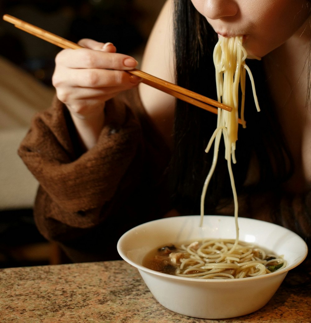 a woman eating a bowl of noodles with chopsticks