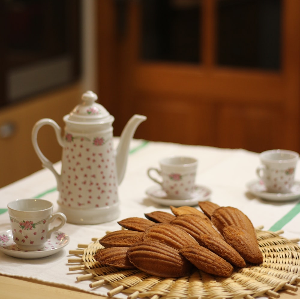a table topped with a basket of cookies next to cups and saucers