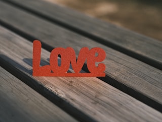A wooden table surface with a red decorative cutout of the word 'Love' placed on it, casting a shadow.