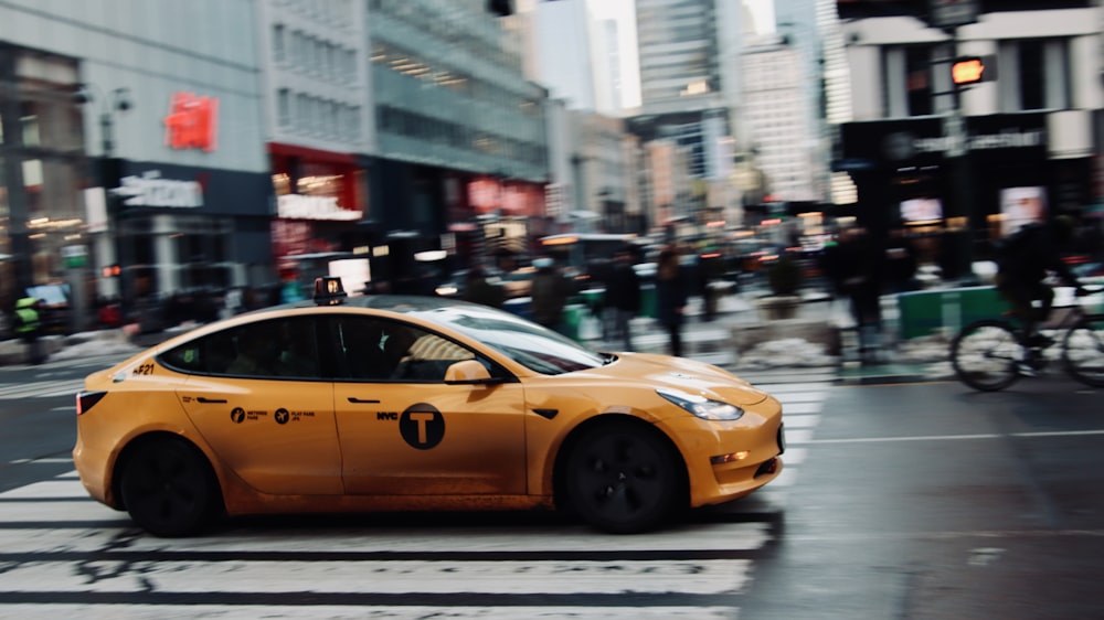 a yellow car driving down a street next to tall buildings