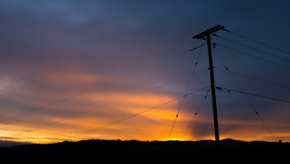 the sun is setting behind a telephone pole