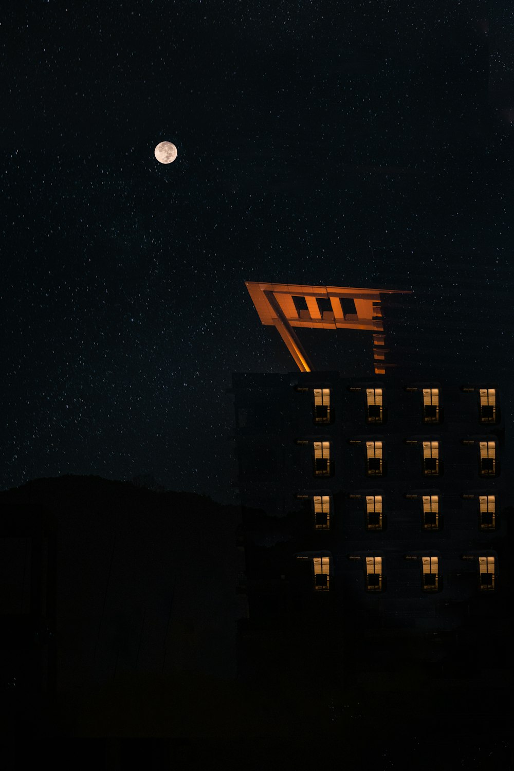 a building is lit up at night with the moon in the sky
