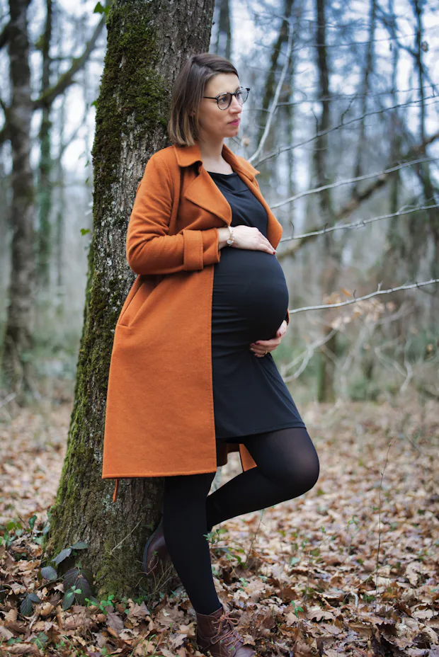 Uma mulher grávida encostada em uma árvore na floresta, em um momento de tranquilidade, simbolizando a importância da saúde materna para o desenvolvimento do bebê.