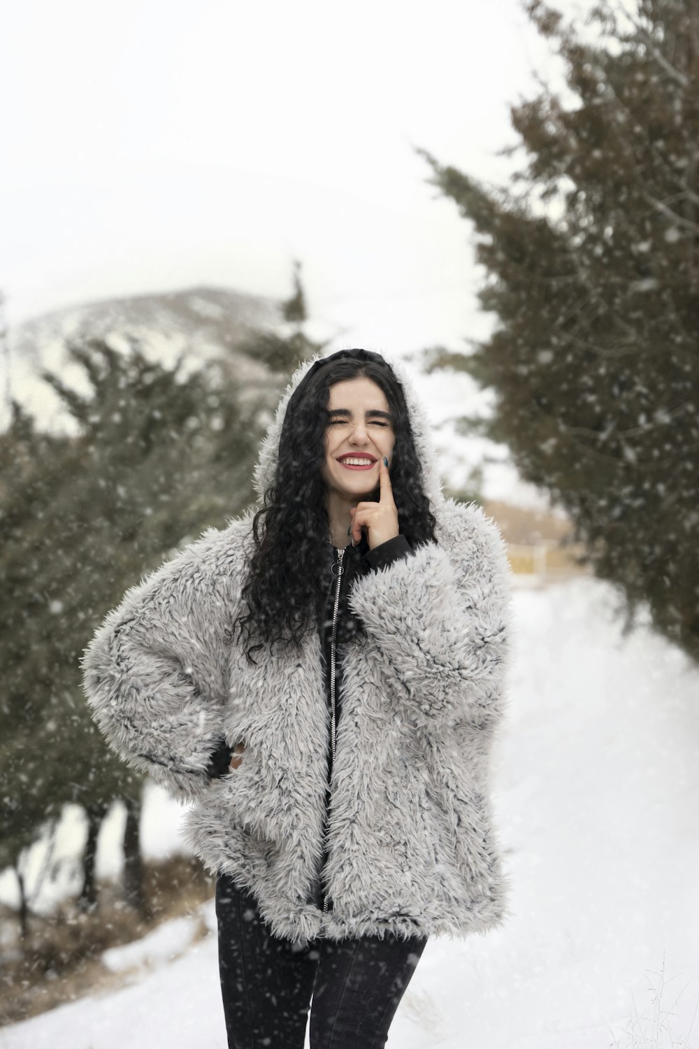 a woman standing in the snow wearing a furry coat