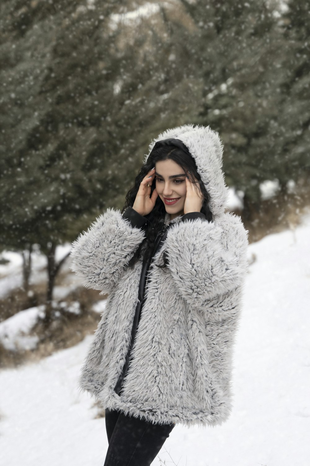 a woman standing in the snow wearing a furry coat