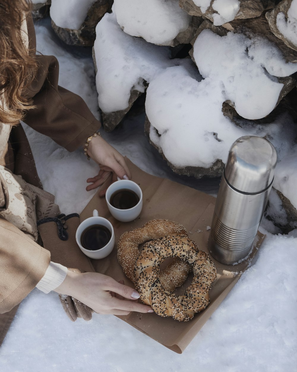 a woman sitting in the snow eating a bagel