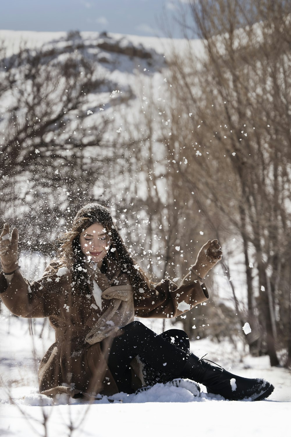 a woman sitting in the snow throwing snow in the air