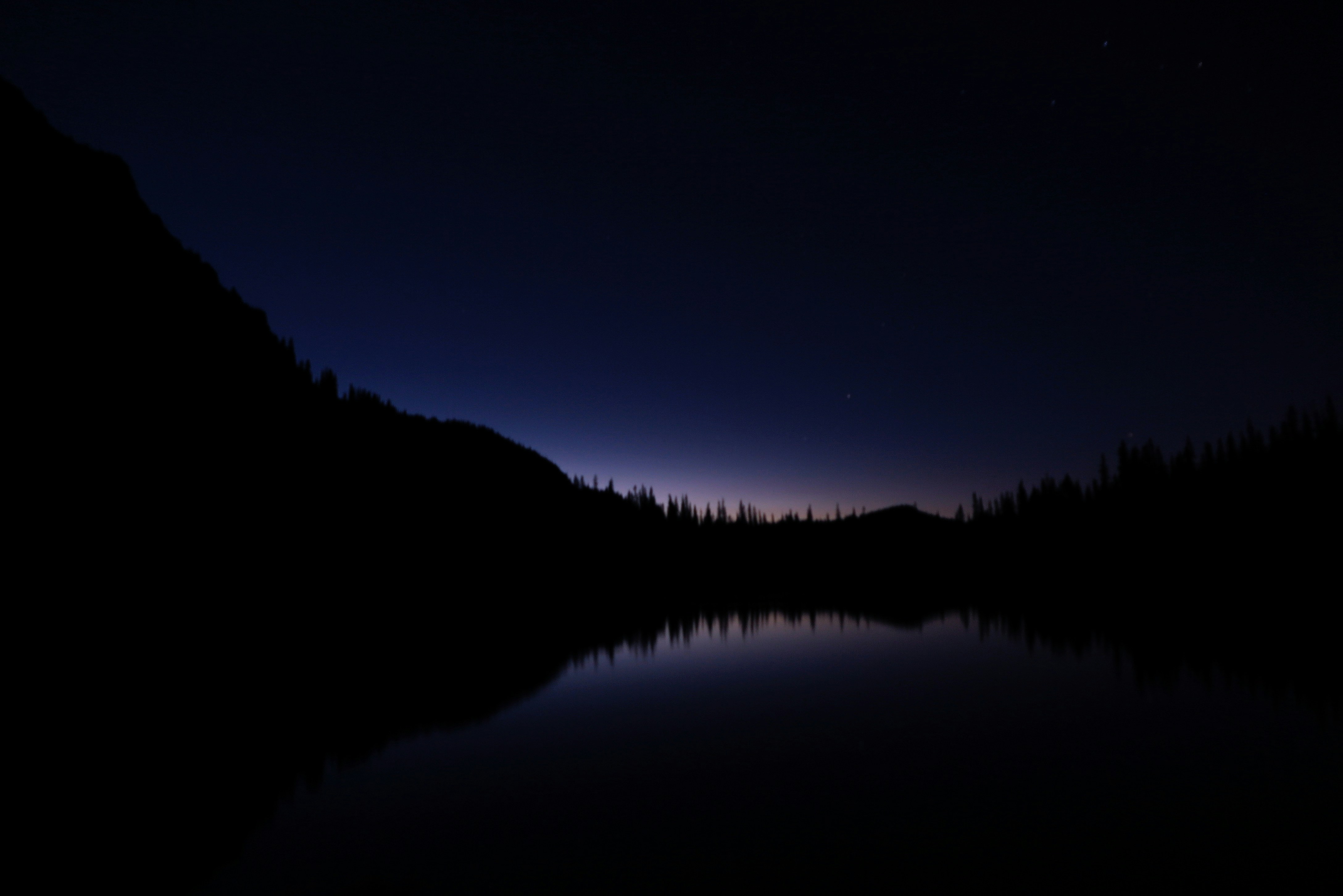 a lake surrounded by a forest under a night sky