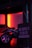 A dimly lit room features a toy car with detailed rims in the foreground, partially illuminated by a red and orange glow. A sign is hanging nearby that reads 'What happens in the man cave stays in the man cave.' The environment suggests a cozy and private atmosphere.