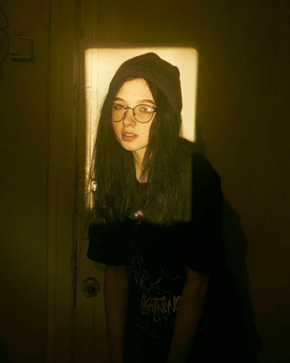 a woman wearing glasses and a hat standing in front of a door