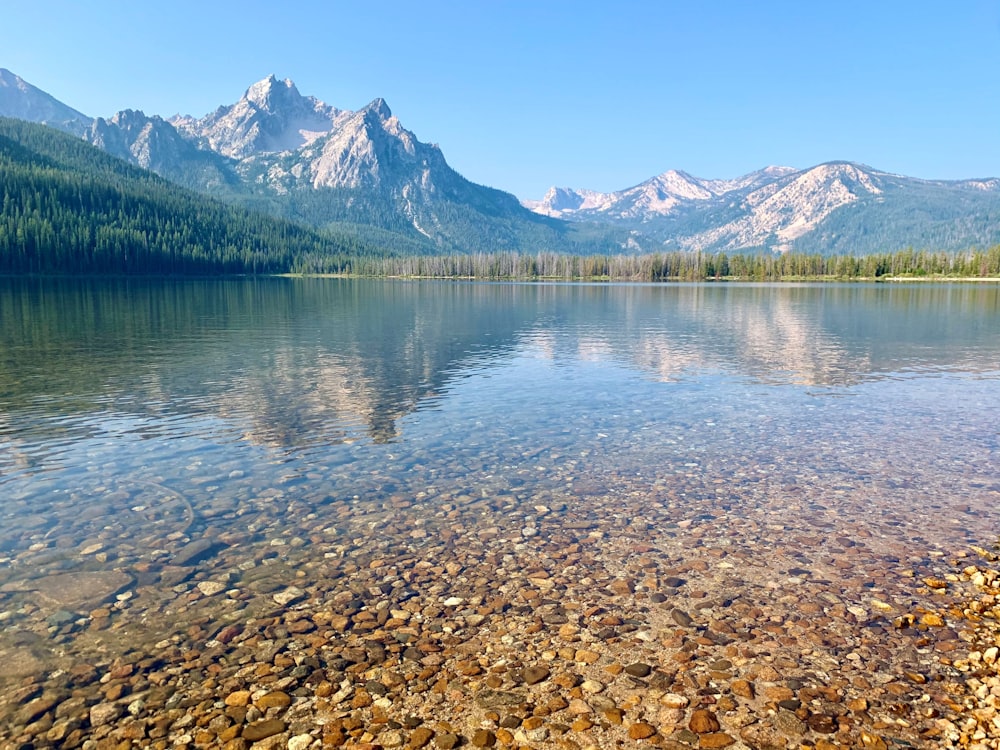 a lake surrounded by mountains with rocks in the water