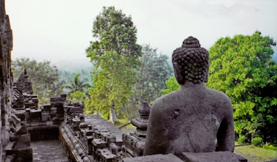 Ancient Buddha statue surrounded by lush greenery and visitors exploring.