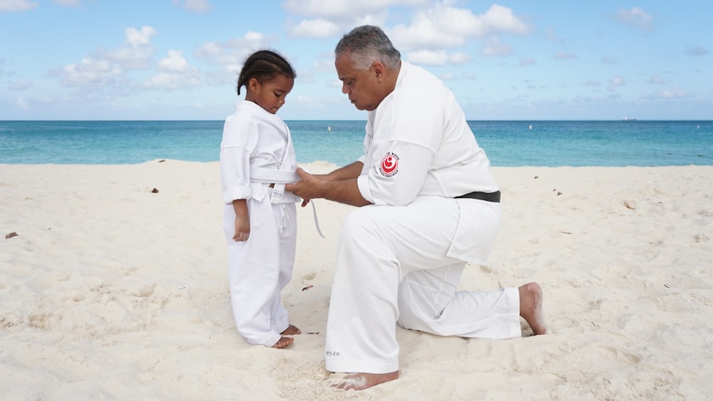 a man kneeling down next to a little girl on a beach