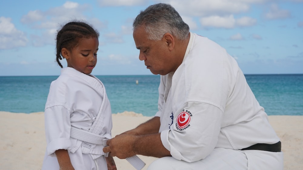 a man kneeling down next to a little girl on a beach