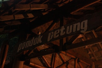 A wooden sign prominently displays the words 'pondok petung' in bold white letters. The background consists of traditional bamboo and wooden architectural elements, creating a rustic and natural aesthetic.