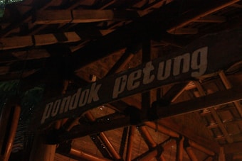A wooden sign prominently displays the words 'pondok petung' in bold white letters. The background consists of traditional bamboo and wooden architectural elements, creating a rustic and natural aesthetic.