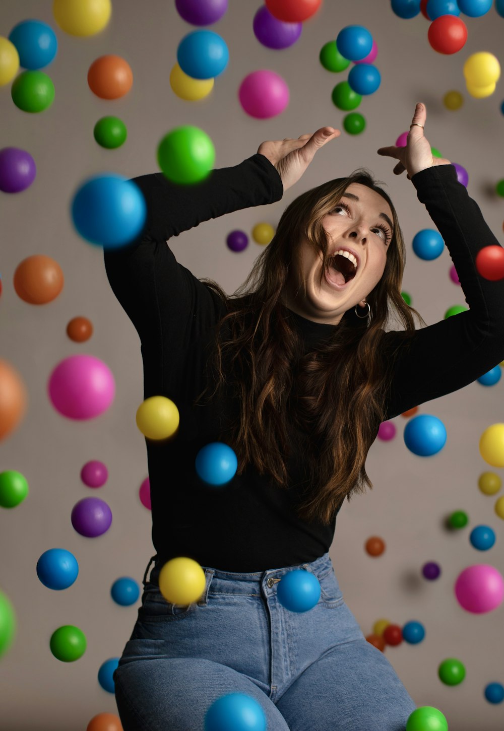 a woman in a black shirt and jeans is surrounded by balloons