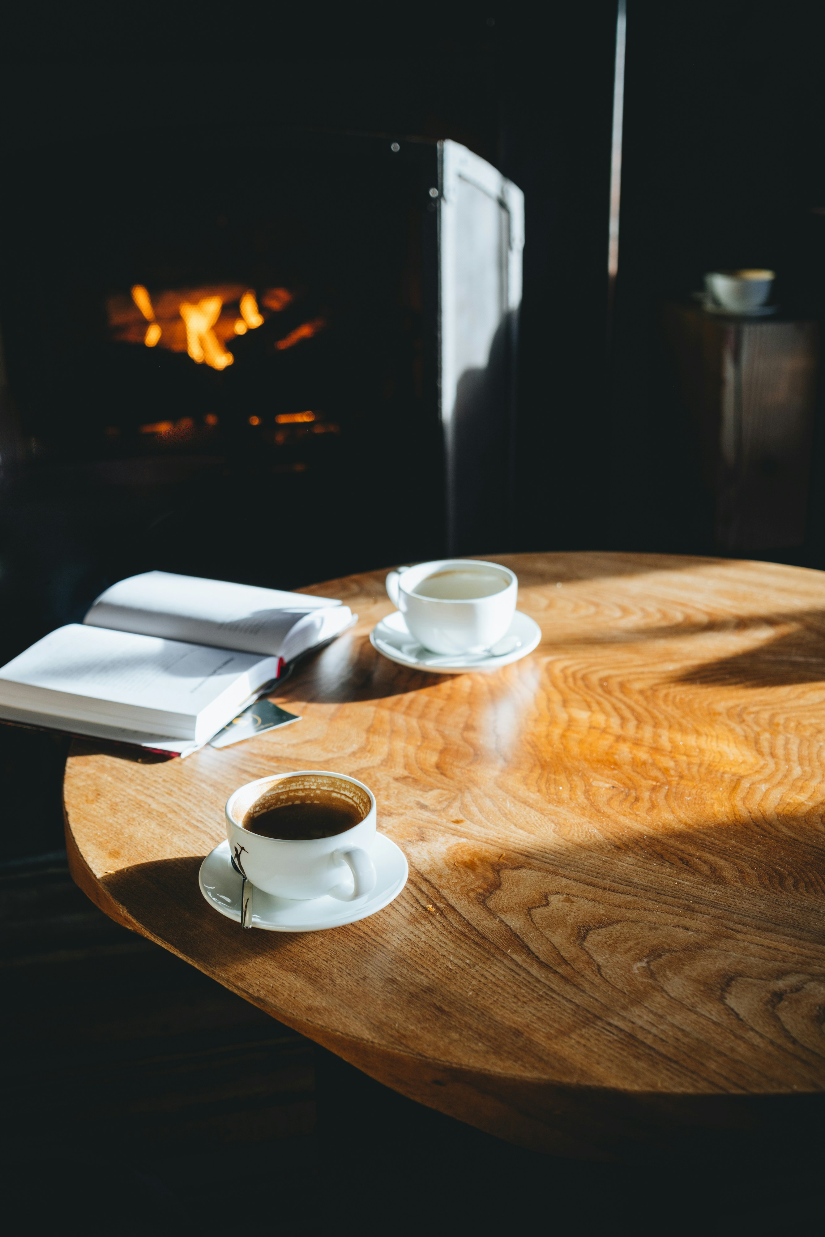 Zwei Kaffeetassen und ein offenes Buch auf einem Holztisch.