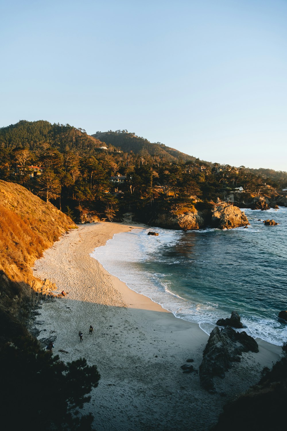 a sandy beach next to a lush green hillside