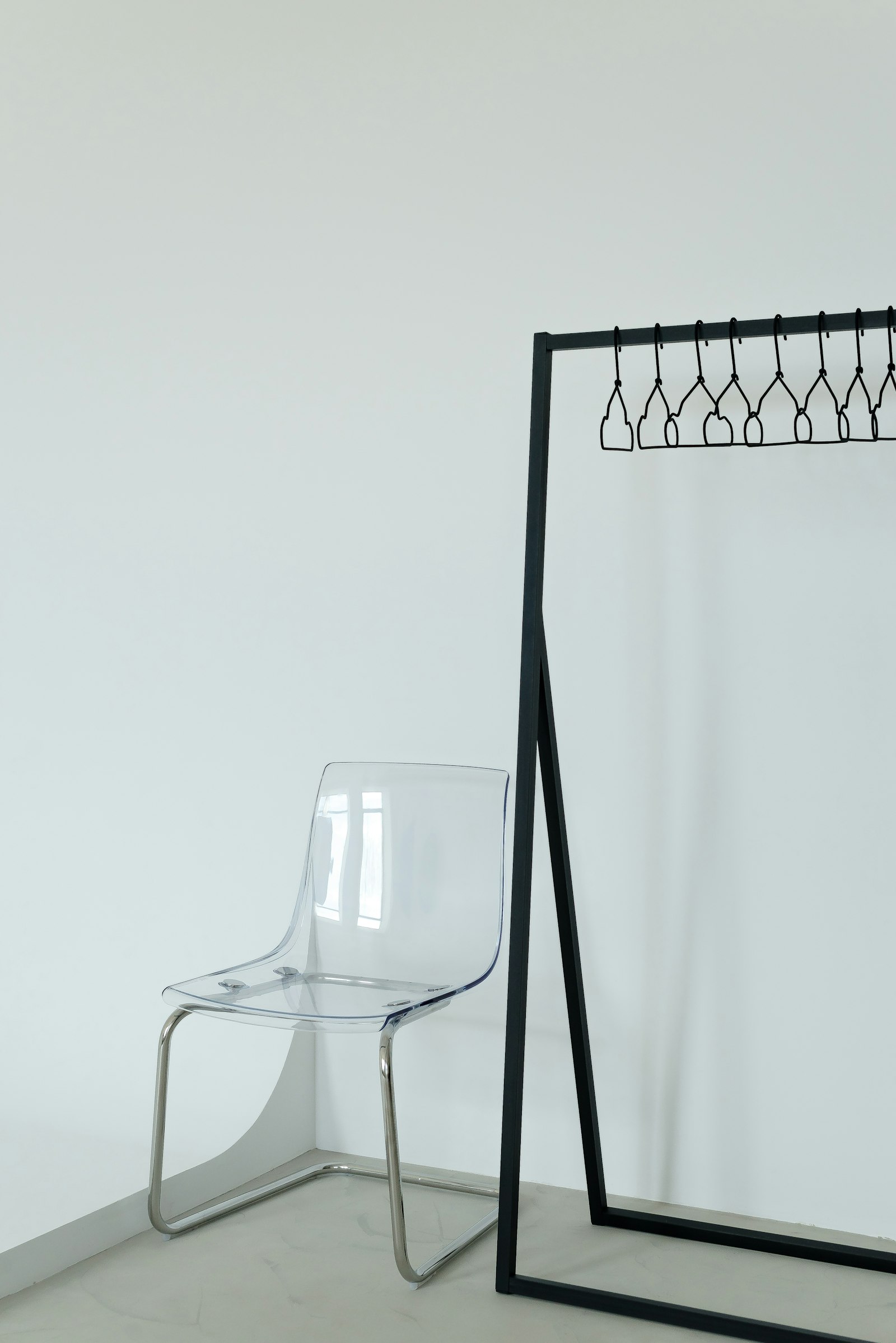 A clear acrylic chair beside a black clothes rail with black hangers in a white room