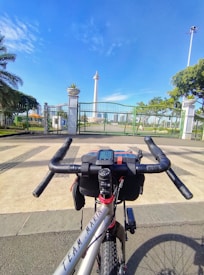 A bicycle with 'Team Marin' branding is positioned in the foreground, facing a fenced area with an iconic tall monument. The structure is surrounded by greenery and blue skies, creating a bright and clear atmosphere.