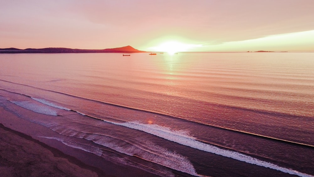 the sun is setting over the water at the beach