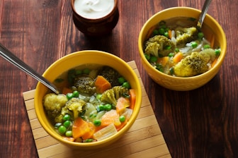 two bowls of soup with peas, carrots and broccoli