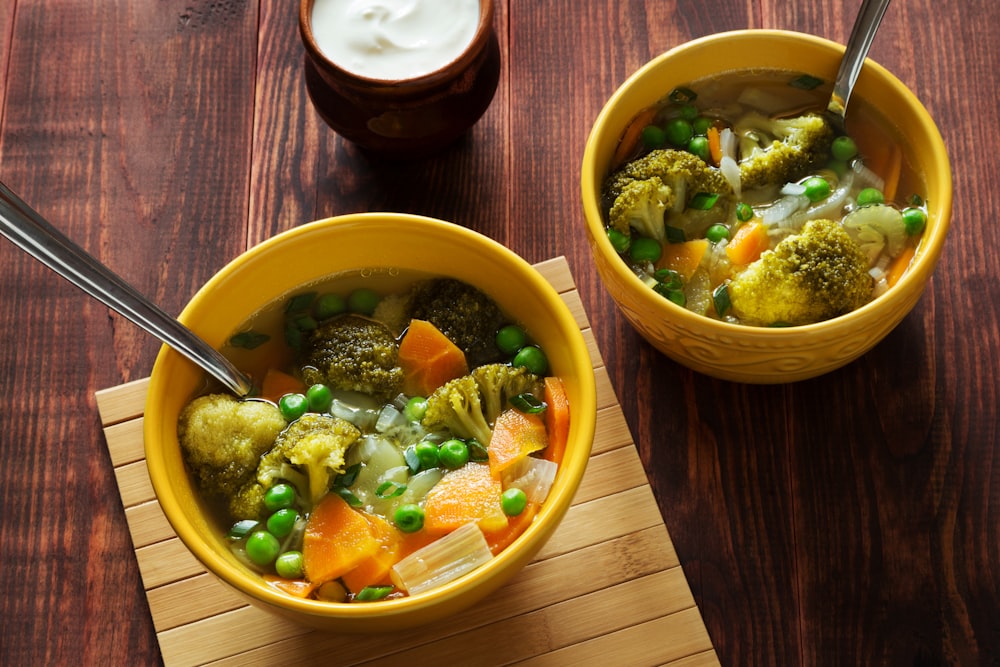 two bowls of soup with peas, carrots and broccoli