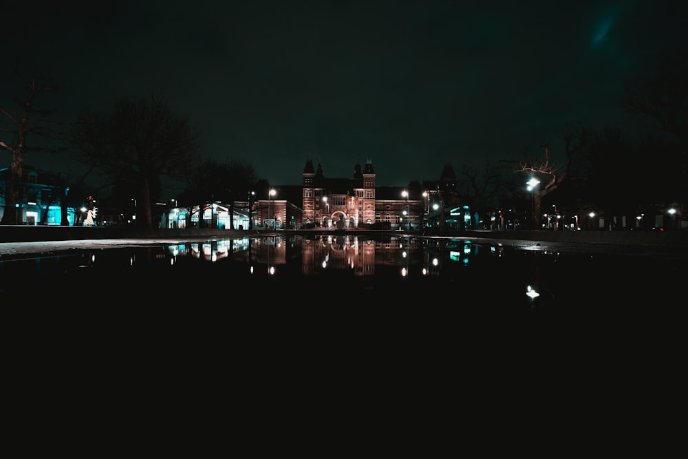a night scene of a large building with a pond in front of it