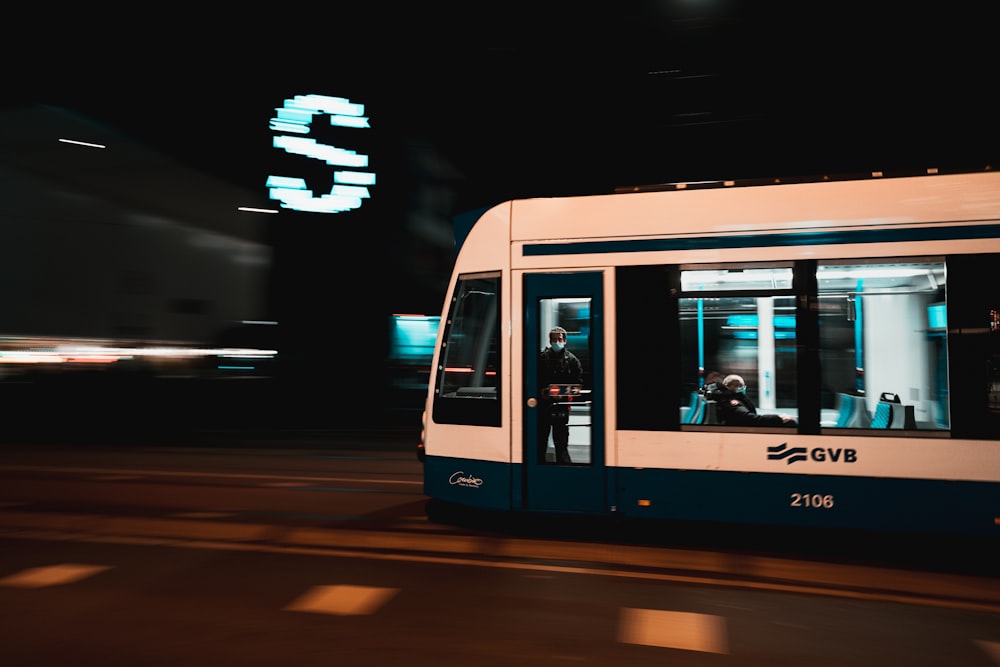 a blue and white train traveling down a street at night