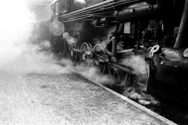 A vintage photograph of an early steam engine in operation, with steam billowing around it.