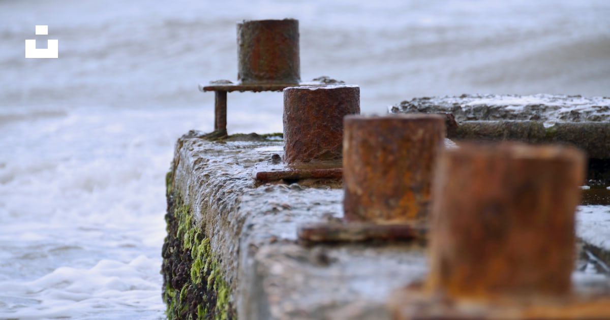 A rusted out bench sitting on the side of a body of water photo – Free ...