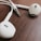 White earphones with a 3.5 mm audio jack placed on a wooden surface. The earphones have a smooth, streamlined design and the jack has a metallic finish with several sections.