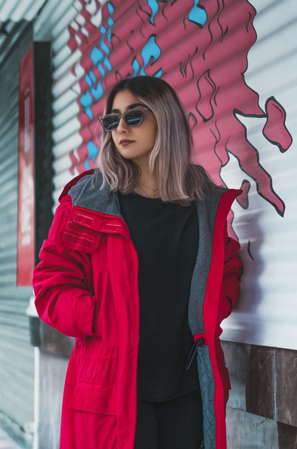 a woman in a red coat leaning against a wall