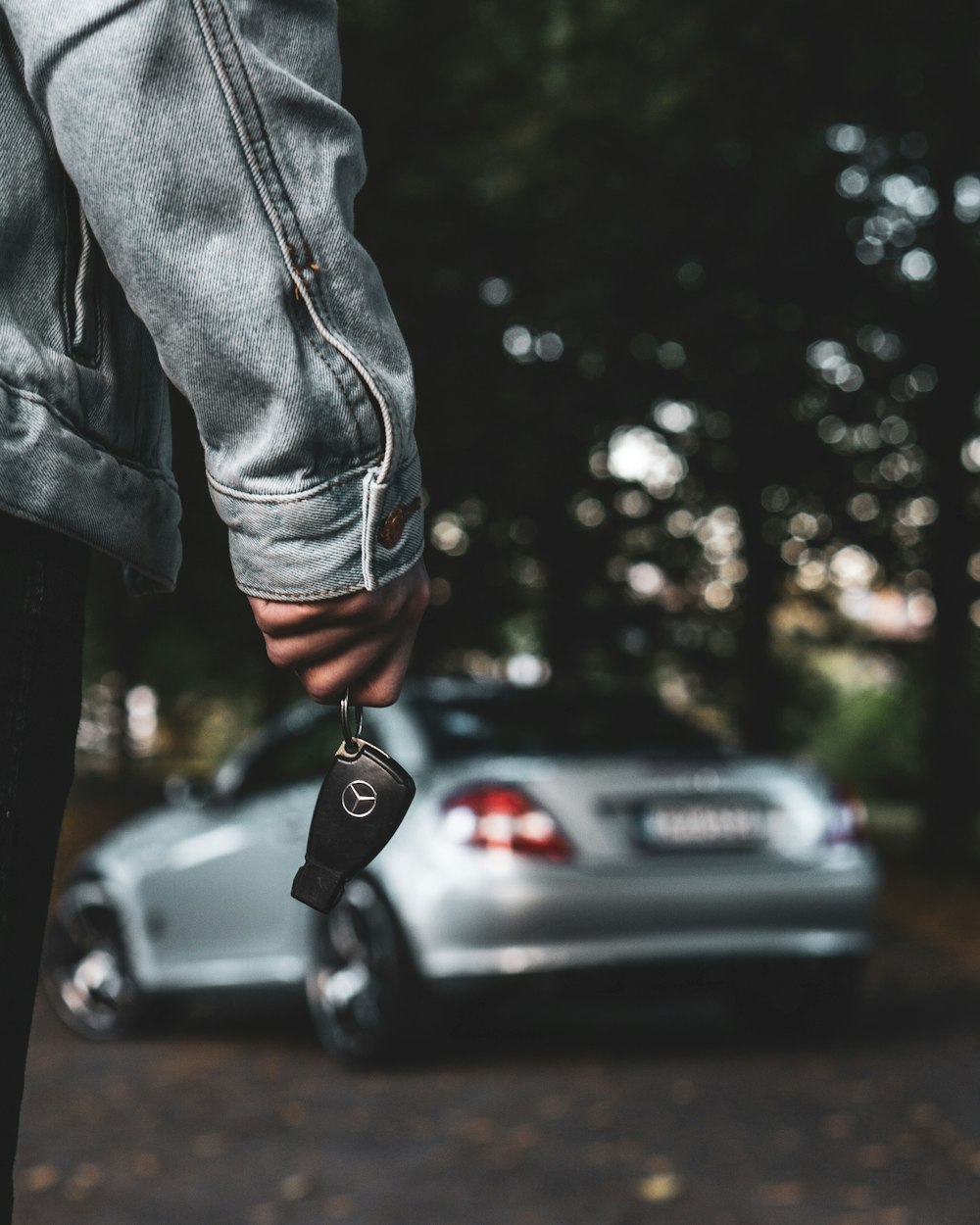 Eine Person, die einen Autoschlüssel neben einem silbernen Auto hält