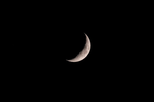 A crescent moon is prominently featured against a stark black sky, showcasing detailed craters along its illuminated edge.