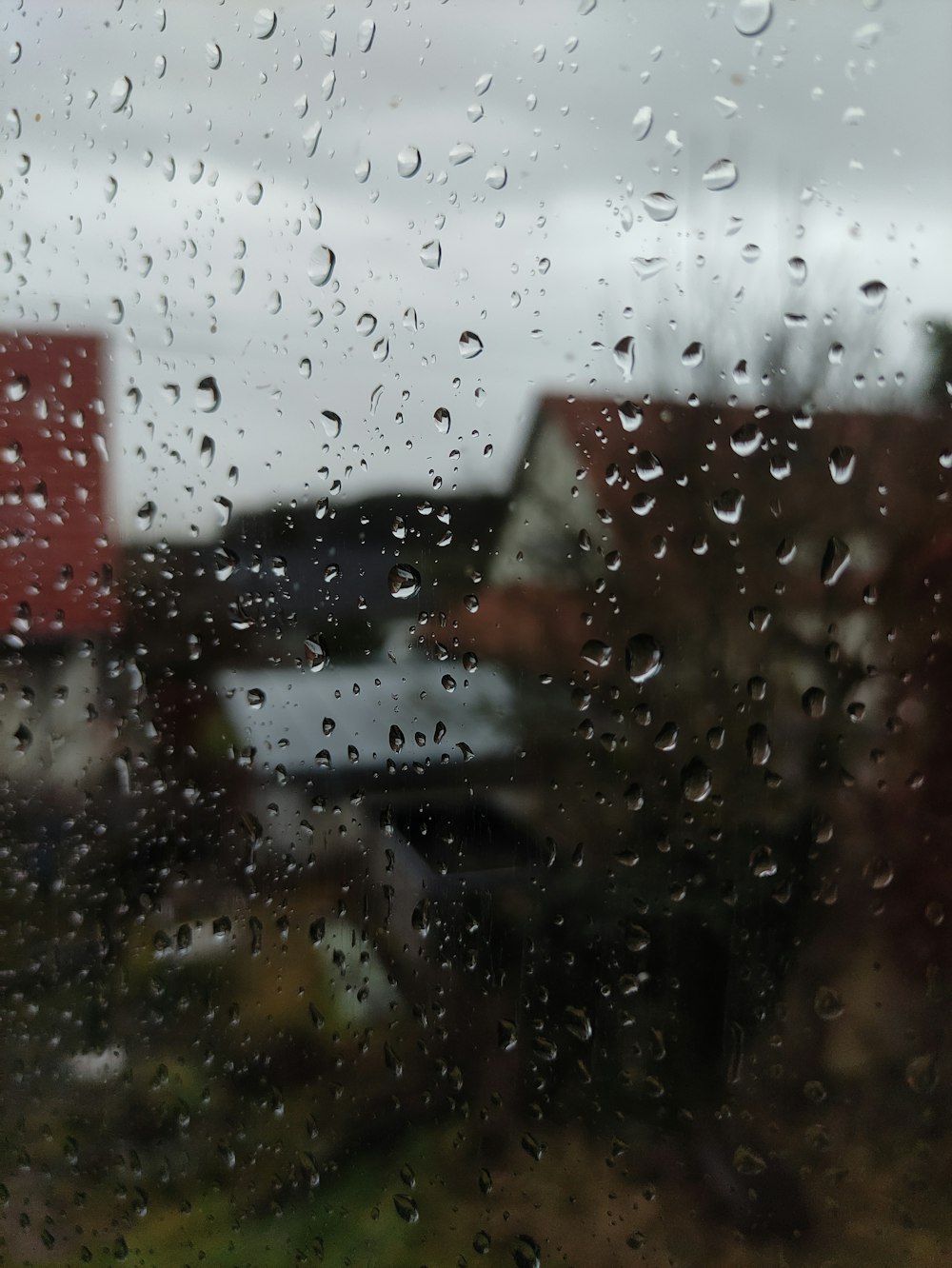 a rain covered window with a red house in the background