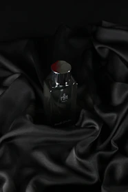 A sleek black bottle of Vedora men's perfume with gold accents resting on a dark marble surface.