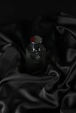 A sleek matte black perfume bottle with matte gold accents resting on a charcoal gray surface under soft cinematic lighting.