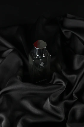 A sleek black matte perfume bottle with brushed silver accents on a dark reflective surface.