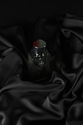 Close-up of a sleek black perfume bottle with gold accents on a dark reflective surface.